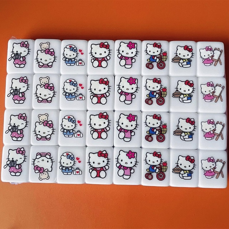 May include: A set of 36 white dominoes with Hello Kitty themed illustrations. Each domino features a different Hello Kitty design, including Hello Kitty taking pictures, riding a bike, baking a cake, and painting.