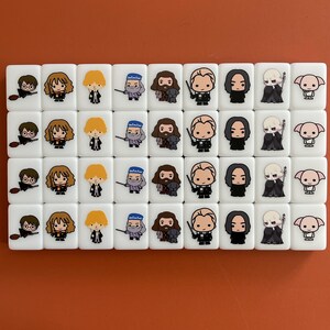May include: Set of 36 white ceramic tiles with Harry Potter characters. Each tile features a different character from the Harry Potter series, including Harry Potter, Ron Weasley, Hermione Granger, Draco Malfoy, and more. The tiles are perfect for playing games or decorating a Harry Potter themed room.