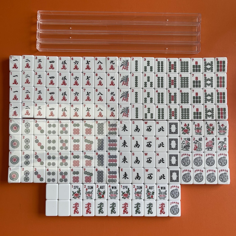 May include: A set of 144 white mahjong tiles with black and red markings. The tiles are arranged in rows and columns, with the numbers 1 through 9, the characters 'East', 'South', 'West', 'North', and 'Wind', and the words 'Spring', 'Summer', 'Autumn', and 'Winter'. There are also four joker tiles.