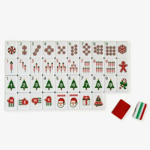 Op de afbeelding: Een set witte rechthoekige mahjongtegels met kerstthema-afbeeldingen, waaronder pepermuntjes, vuurwerk, kerstbomen, wanten, kerstmangezichten, cadeautjes, klokken en peperkoekmannetjes, inclusief twee blanco tegels in rood en gestreept patroon.