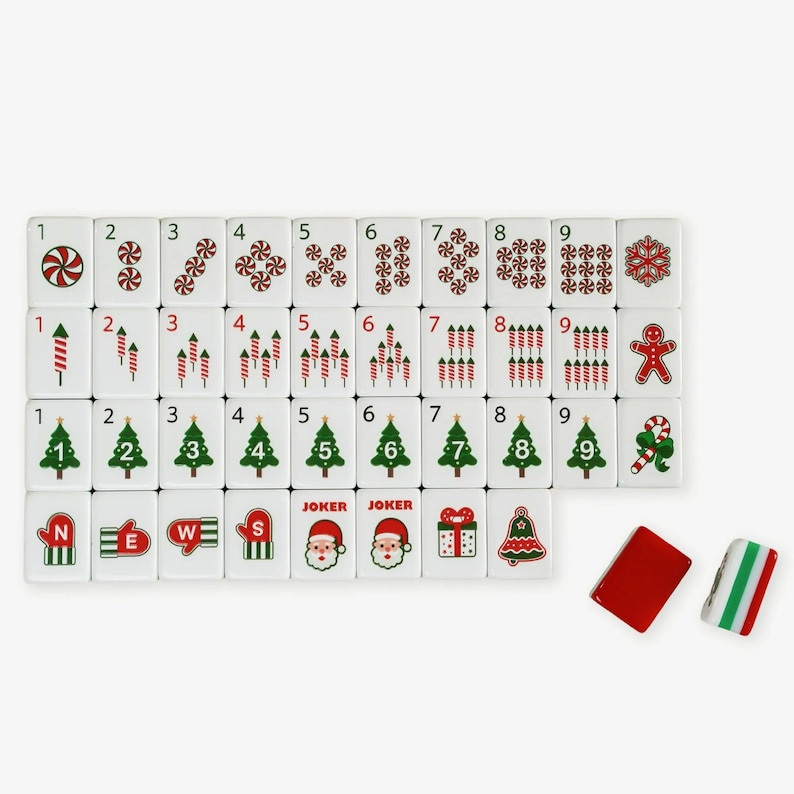 Op de afbeelding: Een set witte rechthoekige mahjongtegels met kerstthema-afbeeldingen, waaronder pepermuntjes, vuurwerk, kerstbomen, wanten, kerstmangezichten, cadeautjes, klokken en peperkoekmannetjes, inclusief twee blanco tegels in rood en gestreept patroon.