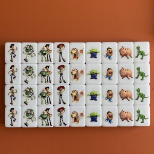 May include: A collection of white rectangular tiles featuring colorful images of characters from the animated film "Toy Story." The tiles display characters like Woody, Buzz Lightyear, and others, arranged in rows.