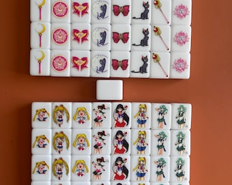 Könnte beinhalten: Ein Satz von 36 weißen Dominosteinen mit Bildern von Charakteren aus dem Anime Sailor Moon. Die Dominosteine zeigen Sailor Moon, Sailor Mercury, Sailor Mars, Sailor Jupiter und Sailor Venus. Die Dominosteine sind in einem Gittermuster angeordnet.