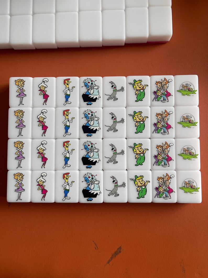 May include: A set of white mahjong tiles featuring cartoon characters. The tiles display colorful illustrations of characters in various poses. The tiles are arranged in rows, with some tiles stacked on top.