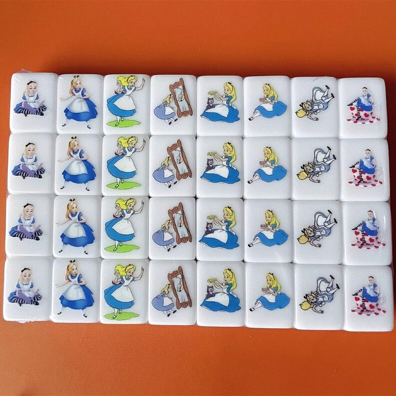 Op de afbeelding: Een set van 24 witte domino's met kleurrijke illustraties van Alice in Wonderland-personages. De domino's tonen Alice, de Cheshire Cat, de Hoedenmaker en de Koningin van harten.
