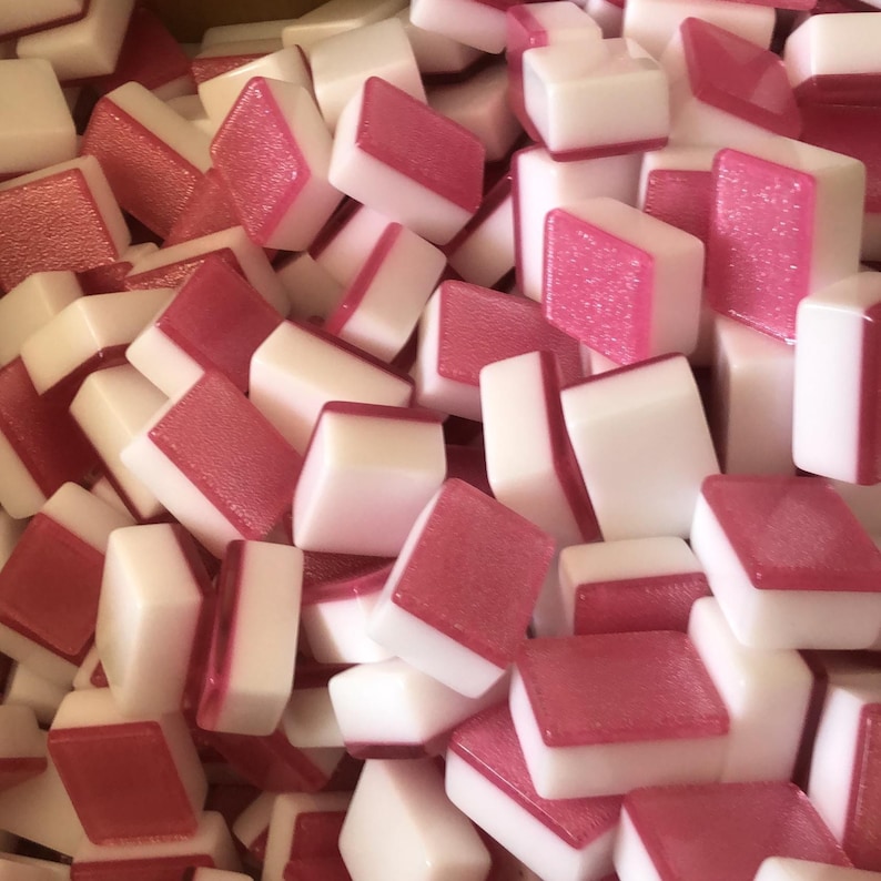 May include: A close-up shot of a pile of white and pink tiles. The tiles are rectangular with a white base and a pink, textured top. The tiles are scattered, creating a visually appealing pattern. The image suggests a game or craft supply.