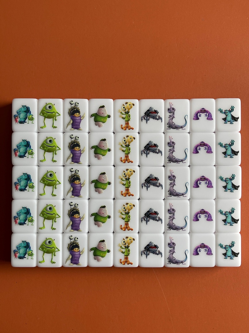Puede incluir: Un conjunto de 36 dados blancos con diferentes personajes de dibujos animados de las pel&iacute;culas de Disney Pixar. Los personajes incluyen Mike Wazowski, Sulley, Boo, Randall y la puerta de Monstruos S.A. Los dados est&aacute;n dispuestos en seis filas de seis dados cada una.