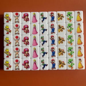 May include: A set of 40 white square tiles with different Mario characters printed on them. The characters include Mario, Luigi, Peach, Toad, Bowser, and Yoshi.
