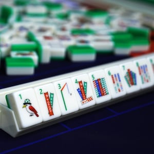 Puede incluir: Un conjunto de fichas de Mahjong blancas y verdes dispuestas en un soporte. La fila frontal muestra fichas numeradas del uno al ocho, con ilustraciones coloridas de un p&aacute;jaro, cintas con el texto Go USA, un bal&oacute;n de f&uacute;tbol y patrones de rayas.