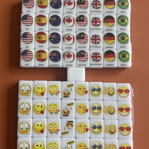 May include: A set of white square tiles with different country flags and emoji faces printed on them. The flags include the United States, Spain, Australia, Canada, Malaysia, United Kingdom, Germany, and Brazil. The emoji faces include a crying face, a tongue sticking out face, a heart eyes face, a surprised face, a thumbs up face, and a sunglasses face.