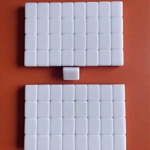 May include: Two white rectangular tiles made of small white squares. The top tile has 6 rows of 7 squares and the bottom tile has 7 rows of 7 squares. The tiles are separated by a single white square.