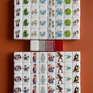 May include: A set of white mahjong tiles with cartoon characters from Rick and Morty and Futurama. The tiles are decorated with colourful illustrations and are arranged on an orange surface.