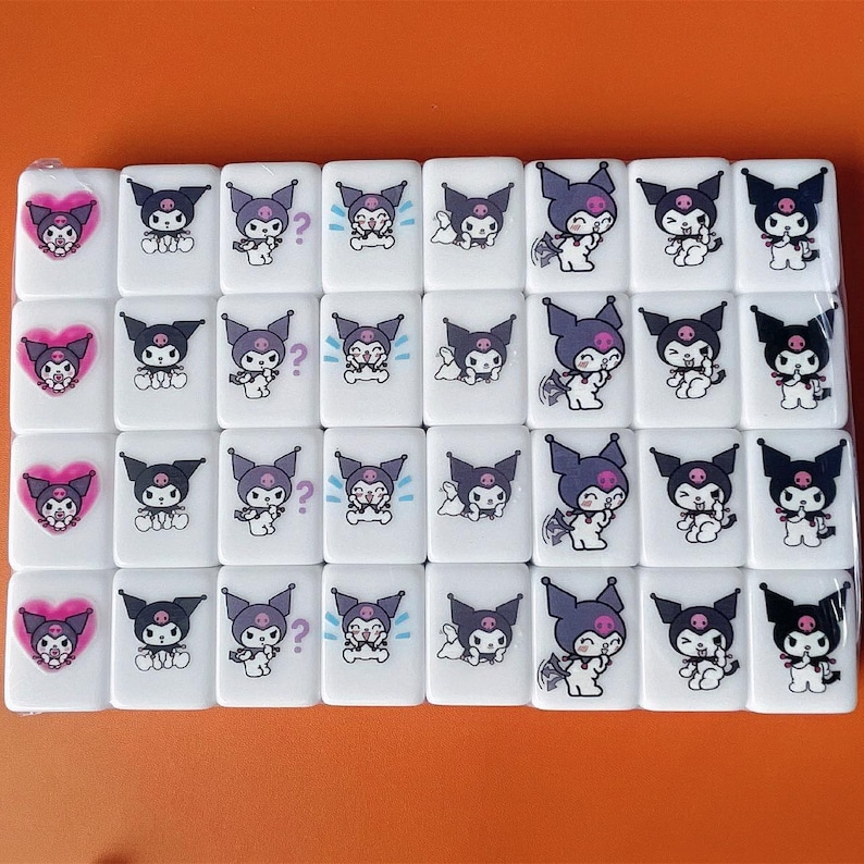 Puede incluir: Un conjunto de 36 fichas de cer&aacute;mica blanca con personajes de dibujos animados negros y morados. Los personajes tienen diferentes expresiones y est&aacute;n dispuestos en una cuadr&iacute;cula.