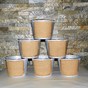 Peut inclure: Six jardinières en métal galvanisé avec un panneau en toile de jute. Les jardinières sont disposées en forme de pyramide. Les jardinières ont une finition argentée avec un bord noir. Le panneau en toile de jute est rectangulaire.