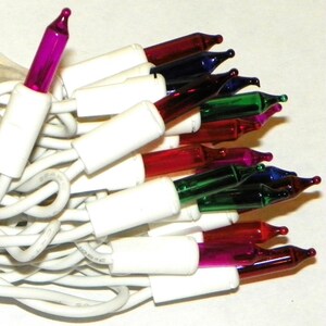 May include: A close-up of a string of Christmas lights with a white wire. The lights are a mix of colors, including red, green, blue, and purple. The bulbs are small and teardrop-shaped.