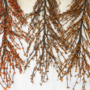 May include: Three artificial floral stems with brown branches and small orange and yellow berry-like accents. The stems are arranged against a white background, creating a visually appealing display for home decor.
