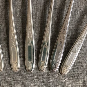 May include: Six silver spoons with ornate designs on the handles. The spoons have a rectangular space on the handle where a name or inscription could be engraved.