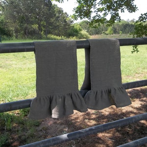 May include: Two gray linen tea towels with a ruffled edge hanging on a black metal fence.