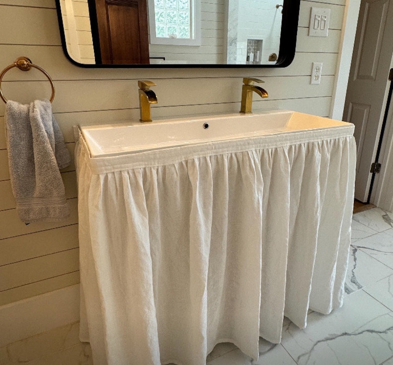 A white linen sink skirt covers a white porcelain bathroom sink. Velcro adhesive curtain are custom made for your sink. please contact me