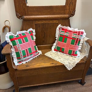May include: Two square throw pillows featuring a patchwork pattern of red and white gingham, green polka dots, and floral ribbon accents. Each pillow is finished with a white ruffled border along the edges, creating a decorative square cushion.
