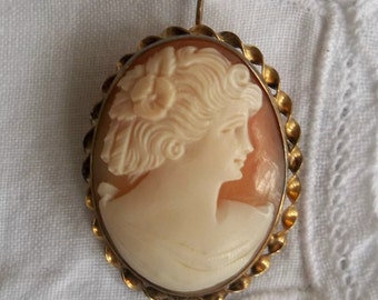 May include: A gold-toned cameo pendant featuring a carved profile of a woman with a detailed hairstyle. The cameo is set in a twisted rope-like frame.