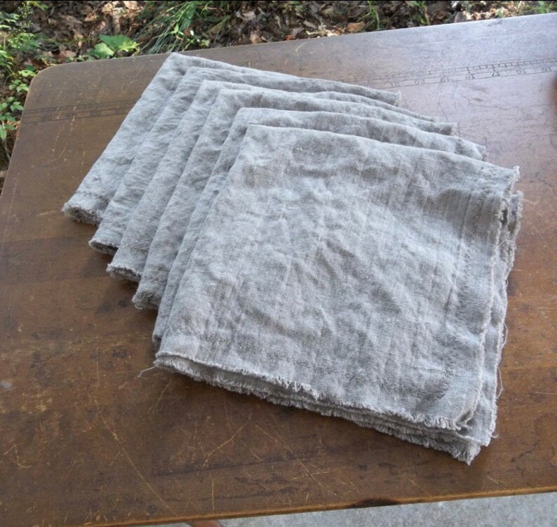 May include: A stack of six gray linen napkins with frayed edges.
