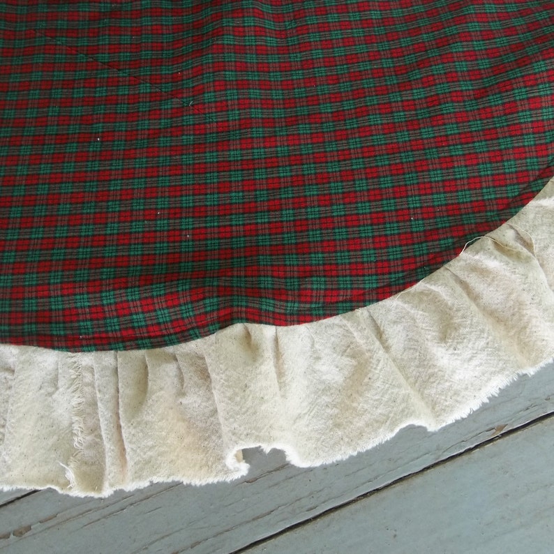 May include: Red and green plaid Christmas tree skirt with a white ruffled edge.