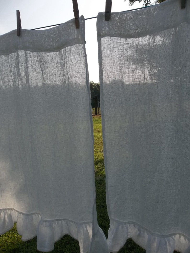 Może przedstawiać: Dwa białe lniane zasłony z falbankami wiszące na sznurze do suszenia. Zasłony są przezroczyste i przepuszczają światło.