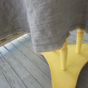 May include: A yellow wooden table with three legs and a gray linen tablecloth draped over it.