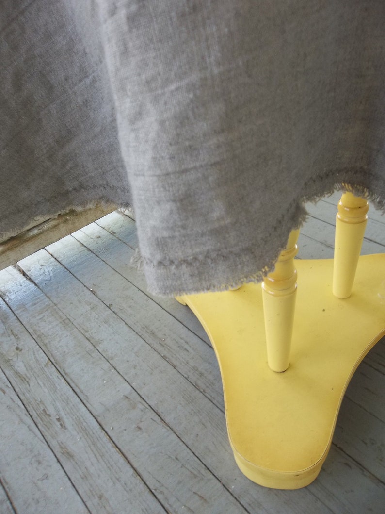 May include: A yellow wooden table with three legs and a gray linen tablecloth draped over it.