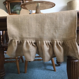 May include: A brown burlap table runner with a ruffled edge. The runner is draped over a wooden table and chairs.