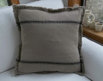 May include: A gray and black striped pillow with a frayed edge. The pillow is sitting on a white couch.