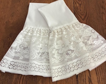 May include: Two white pillowcases with a decorative lace trim. The lace features floral and geometric patterns, adding a delicate touch to the bedding. The pillowcases are made of a smooth, white fabric.