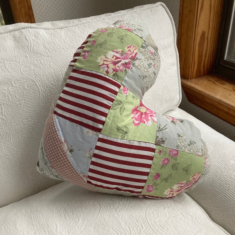 May include: A heart-shaped patchwork pillow with a variety of floral and striped patterns in shades of red, green, and blue.