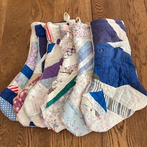 May include: A collection of five handmade Christmas stockings. Each stocking is made from a patchwork of various fabrics in shades of blue, white, purple, and red. The stockings have a quilted appearance and are arranged on a wooden surface.