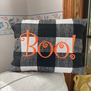 May include: Black and white buffalo check pillow with the word "Boo!" embroidered in orange.
