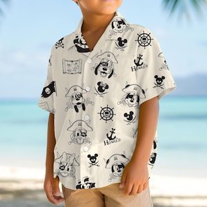 May include: A short-sleeved, button-down shirt with a pirate theme. The shirt features a cream-colored background with black illustrations of pirate-themed characters, including Mickey Mouse, Pluto, and pirate symbols like skulls, anchors, and treasure maps.