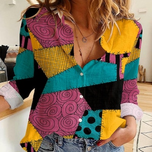 May include: A patchwork-style button-down shirt with long sleeves. The shirt features a vibrant mix of colors and patterns, including teal, yellow, black, and pink. The design incorporates swirls, polka dots, and cross-stitch details, creating a unique and eye-catching look.