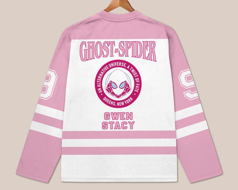 May include: Pink and white Ghost-Spider hockey jersey. The jersey features the text "GHOST-SPIDER" above a circular emblem with a spider-themed mask and the text "AN ALTERNATIVE UNIVERSE, A TWIST OF FATE, QUEENS, NEW YORK". The name "GWEN STACY" is below the emblem.