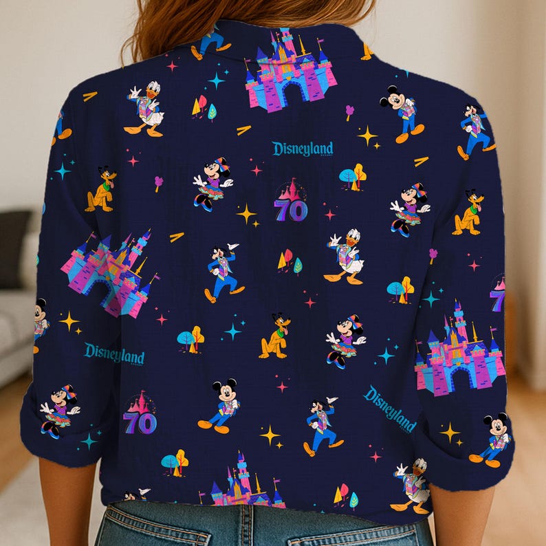 May include: Navy blue button-up shirt featuring a Disneyland theme. The shirt is adorned with colorful illustrations of Mickey Mouse, Donald Duck, and other Disney characters, along with the text "Disneyland" and the number "70".