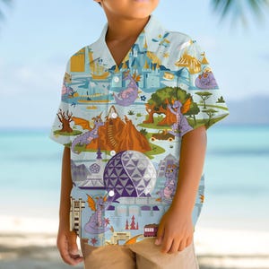 May include: A light blue button-down shirt featuring a colorful cartoon design. The pattern includes castles, mountains, trees, and purple dragons. The shirt has short sleeves and a classic collar.