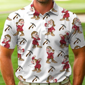May include: White polo shirt featuring a repeating pattern of cartoon dwarves in red outfits and pickaxes. The dwarves have various expressions. The shirt has a collared neckline and short sleeves.