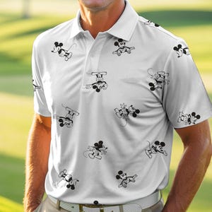 Puede incluir: Polo blanco con un estampado repetido de ilustraciones de Mickey Mouse en blanco y negro. La camisa tiene un cuello cl&aacute;sico, mangas cortas y una tapeta abotonada. La camisa est&aacute; hecha de un material ligero, posiblemente deportivo.