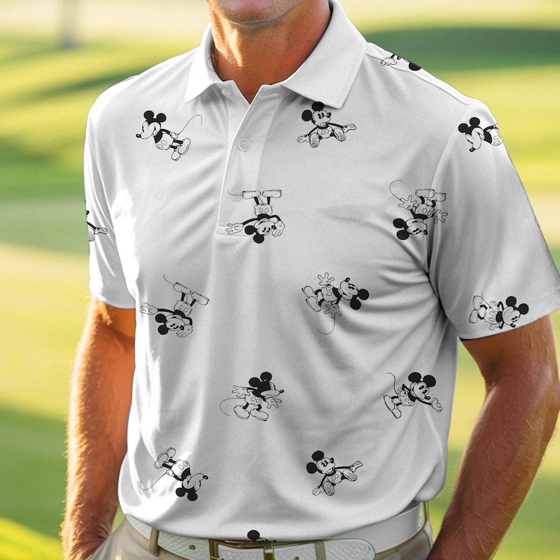 Puede incluir: Polo blanco con un estampado repetido de ilustraciones de Mickey Mouse en blanco y negro. La camisa tiene un cuello cl&aacute;sico, mangas cortas y una tapeta abotonada. La camisa est&aacute; hecha de un material ligero, posiblemente deportivo.