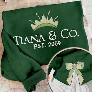 May include: Green sweatshirt with white embroidery that reads "Tiana & Co. Est. 2009" and a green crown above the text. The back of the sweatshirt has a green bow with a yellow center.