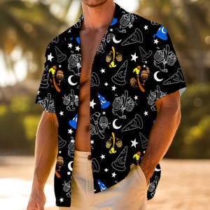 May include: Black button-down shirt with a repeating pattern of white outlined wizard hats, moons, stars, and potion bottles. The shirt has short sleeves and is unbuttoned. The shirt is part of a clothing collection.