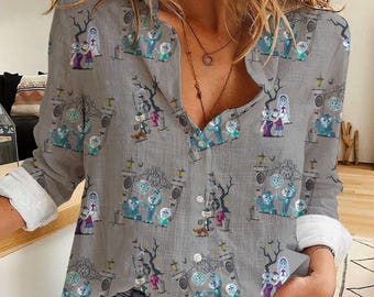 May include: Grey button-down shirt with a Halloween pattern. The design includes cartoon characters, gates, trees, and tombstones in blue, purple, and green. The shirt has long sleeves with white cuffs.