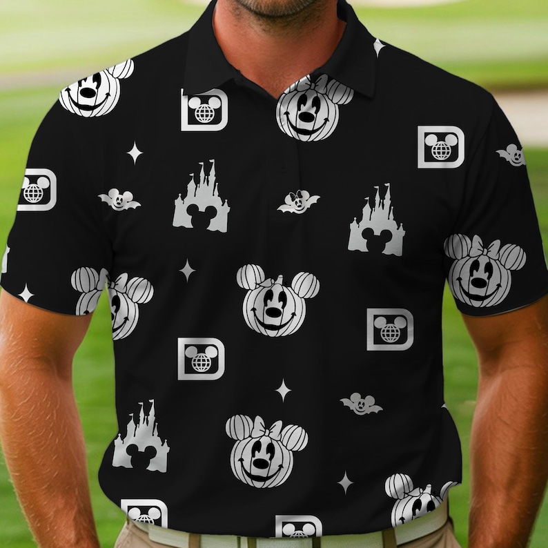 Puede incluir: Polo negro con un estampado repetido en blanco de iconos de Disney, incluyendo calabazas de Mickey Mouse, siluetas de castillos y el logotipo del globo de Disney. La camisa tiene cuello y mangas cortas, adecuada para uso casual.