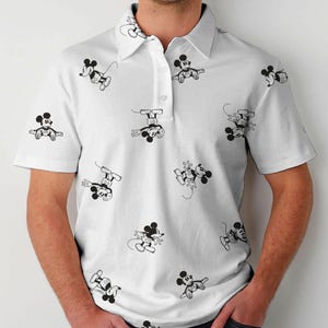Puede incluir: Polo blanco con un patr&oacute;n repetido de ilustraciones de Mickey Mouse en blanco y negro. La camisa de manga corta tiene cuello y tapeta abotonada.