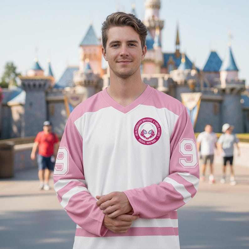 May include: A white and pink hockey-style jersey with the number 9 on the sleeves. The jersey has a V-neck and a circular emblem with text and a graphic. The sleeves have two white stripes. The jersey is worn by a person.